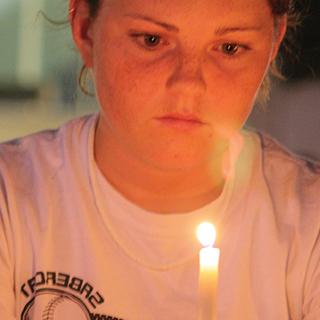 Close up of female TCU student looking thoughtful as she holds a candle before her face.